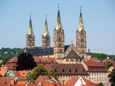 Blick auf eine Stadt mit mehreren Türmen einer Kirche und traditionellen Gebäuden unter klarem Himmel.