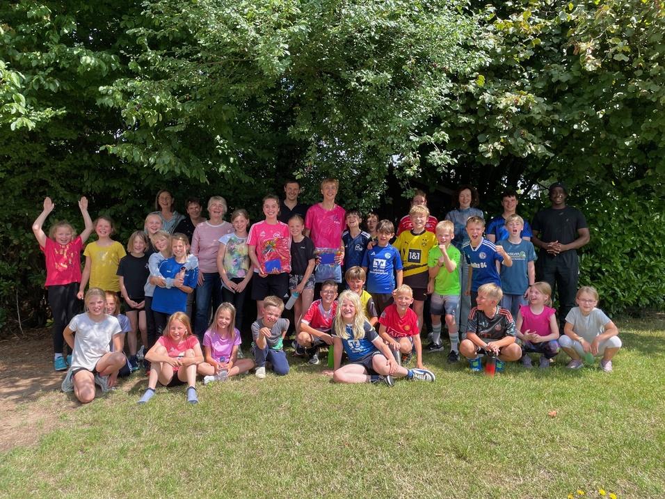 Gruppenshot von Kindern und Jugendlichen in bunten T-Shirts, freudig posierend vor einem Baum.