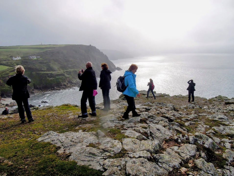 Gruppe von Menschen steht auf einem felsigen Küstenhang und hält Landschaftsaufnahmen am Meer bei bewölktem Himmel fest.