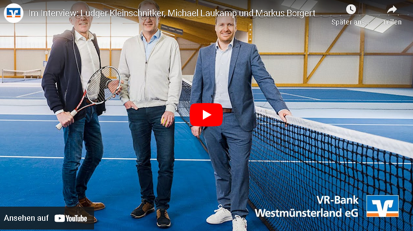 Drei Männer stehen auf einem blauen Tennisplatz neben einem Netz, zwei halten Tennisschläger, einer trägt Anzug.