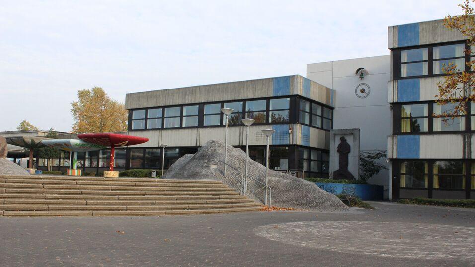 Eingang zu einem Schulgebäude mit Stufen, modernen Lampen und farbenfrohen Skulpturen im Außenbereich.