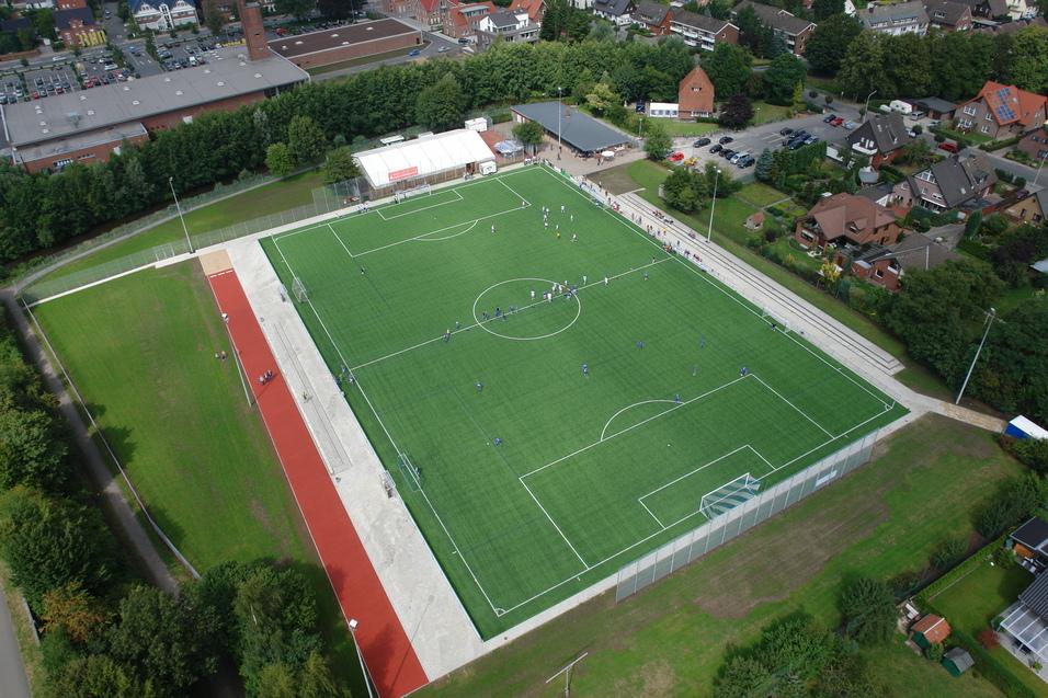 Luftaufnahme eines Fußballplatzes mit Spielern in blauen Trikots und umgebender Wohnbebauung.