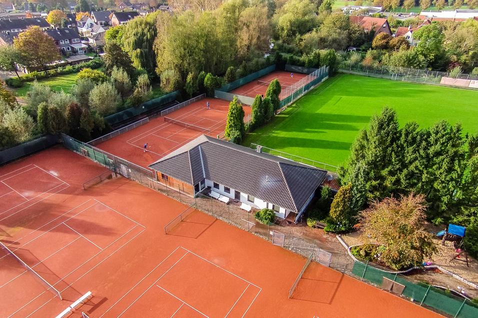 Luftaufnahme einer Tennisanlage mit mehreren roten Sandplätzen und einem Vereinsgebäude im Hintergrund.