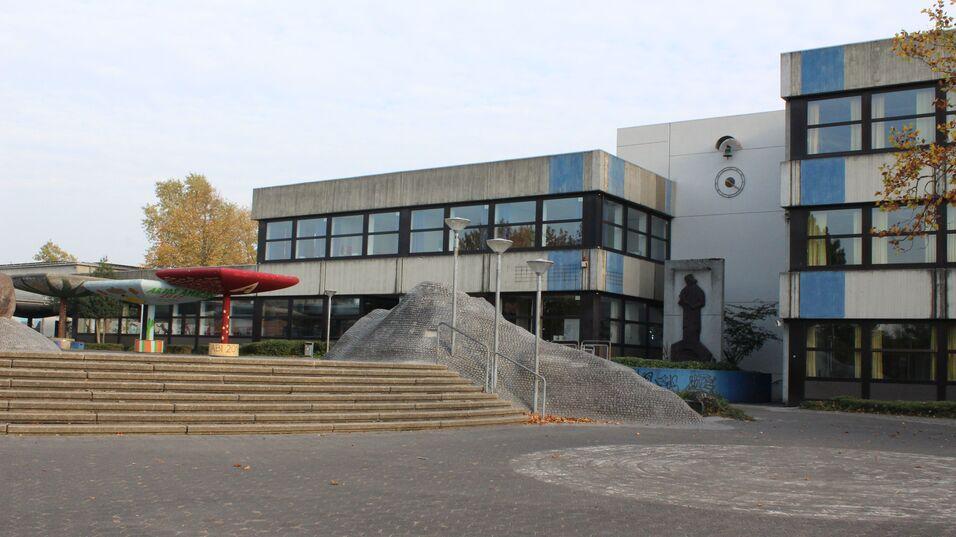 Eingang zu einem Schulgeb&auml;ude mit Stufen, modernen Lampen und farbenfrohen Skulpturen im Au&szlig;enbereich.