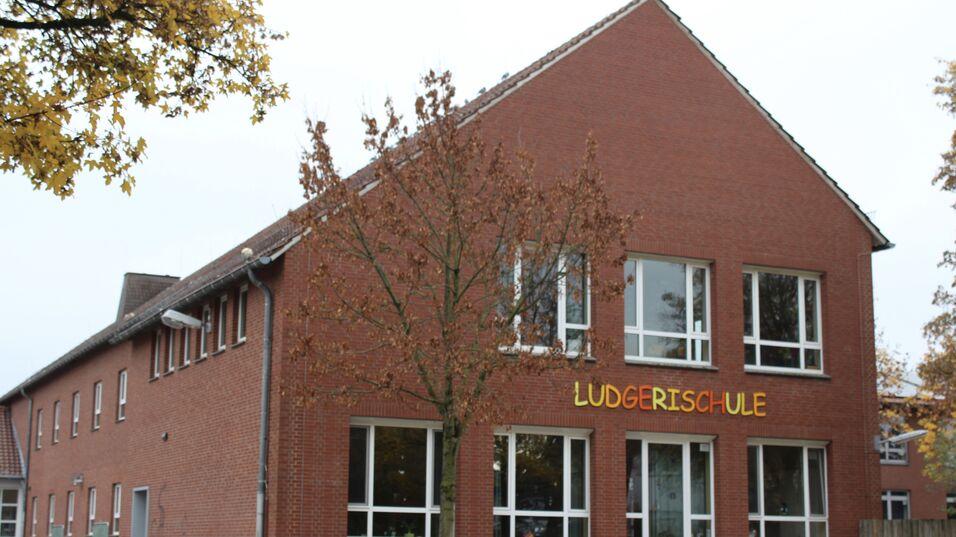Fassade der Ludgerischule mit großen Fenstern und einem Baum im Vordergrund, im Hintergrund sind Fahrräder und Autos sichtbar.