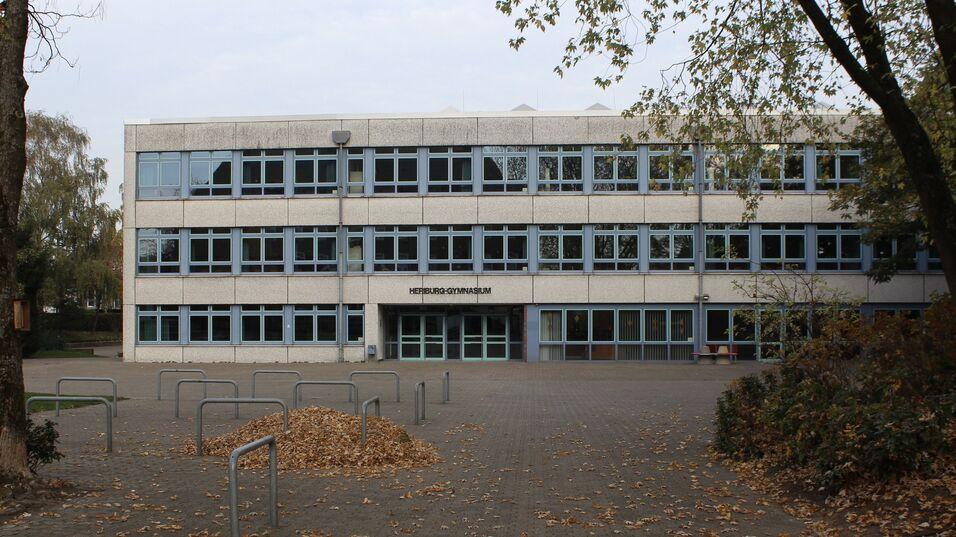 Fassade des Heriburg-Gymnasiums mit großen Fenstern und Laubhaufen auf dem Schulhof.