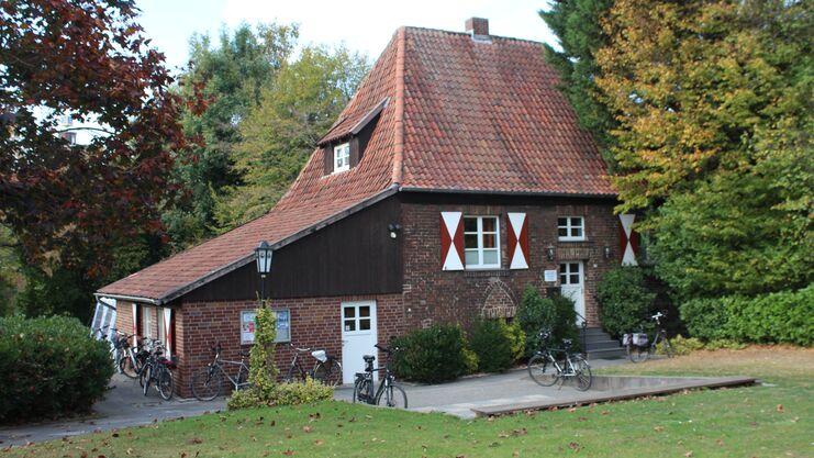 Fachwerkhaus mit rotem Ziegeldach, umgeben von Bäumen und mehreren Fahrrädern auf einem Parkplatz.
