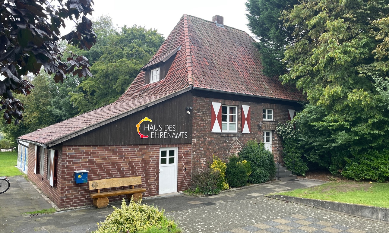 Haus des Ehrenamts, ein zweigeschossiges Gebäude mit rotem Dach, Braune Ziegelwand und Garten, umgeben von Bäumen.