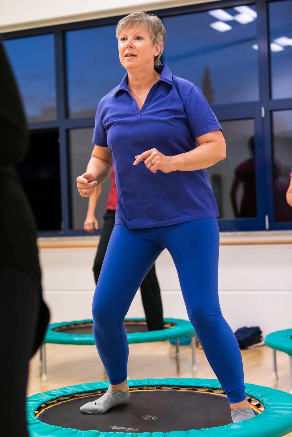 Eine Frau in blauer Sportkleidung springt auf einem Trampolin in einem Fitnessraum.