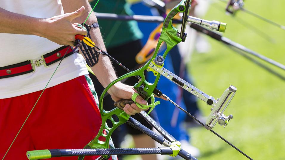 Nahaufnahme einer Hand, die einen grünen Bogen hält, während ein Pfeil mit einer speziellen Halterung geladen wird.