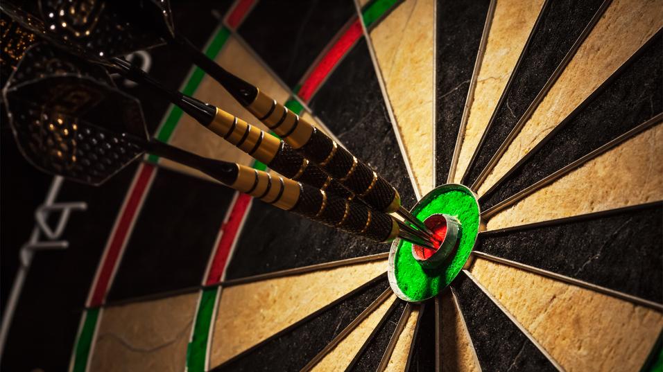 Drei Pfeile stecken im roten Bullseye einer Dartscheibe, umgeben von schwarzen und grünen Feldern.