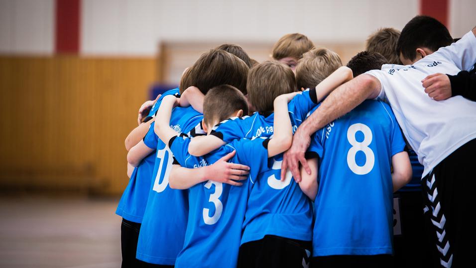 Gruppe junger Sportler in blauen Trikots umarmt sich in einer Halle vor dem Spiel.