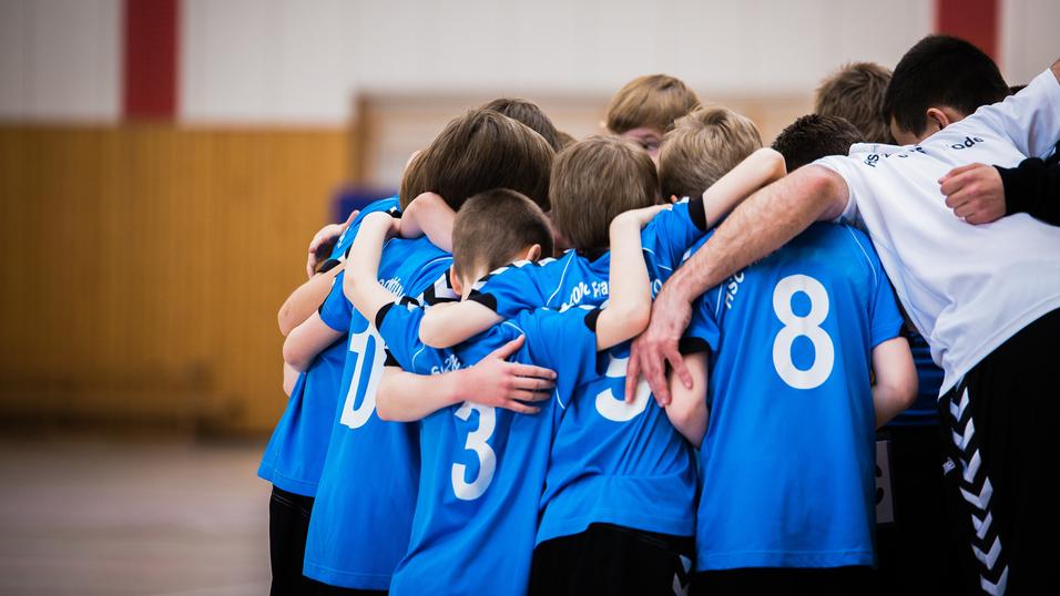 Gruppe junger Sportler in blauen Trikots umarmt sich in einer Halle vor dem Spiel.