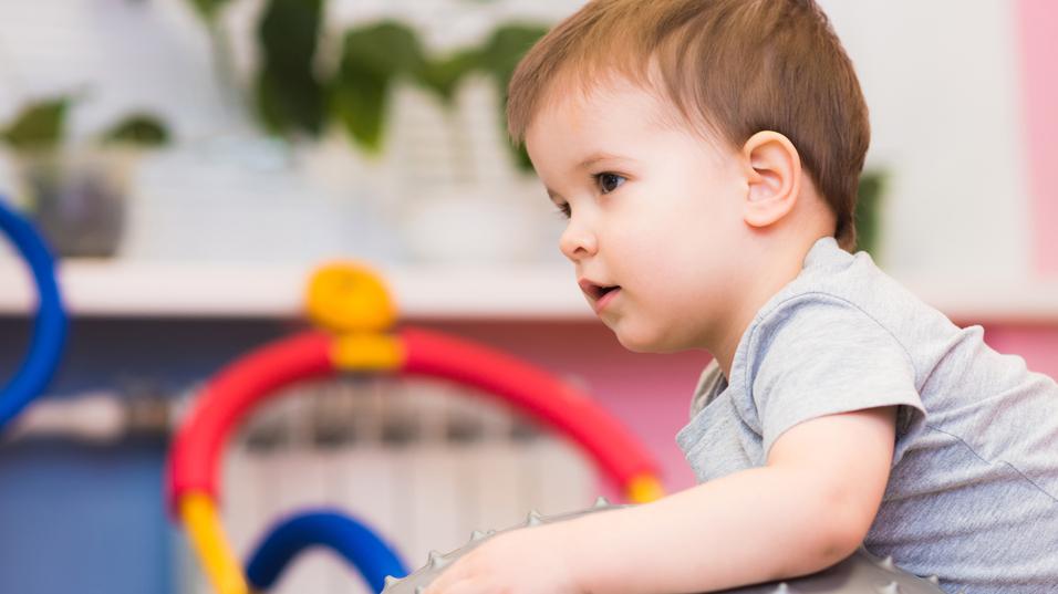 Kleines Kind sitzt auf einem großen, stacheligen Gymnastikball in einem bunten Spielzimmer.
