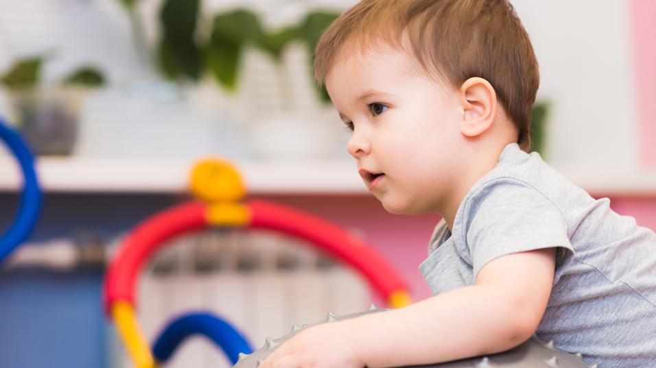 Kleines Kind sitzt auf einem großen, stacheligen Gymnastikball in einem bunten Spielzimmer.
