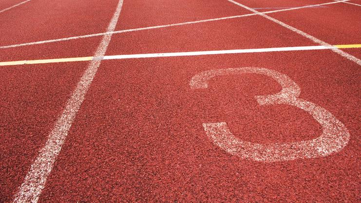 Nahaufnahme eines roten Laufbahnabschnitts mit der Markierung der Bahn 3 und weißen Linien.