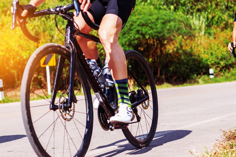 Radfahrer mit gestreiften Socken fährt auf einer Straße, das Vorderrad und Teil des Rahmens sind sichtbar.