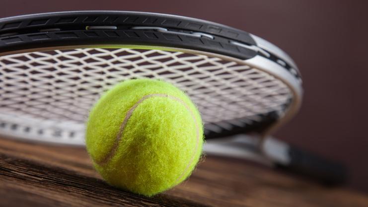 Nahaufnahme eines gelben Tennisballs neben einem Tennisschläger auf einer Holztischoberfläche.