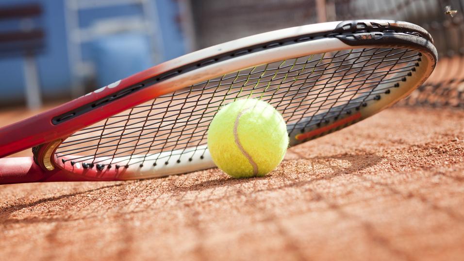 Tennisball liegt auf einem Platz neben einem Tennisracket auf dem Sandboden.