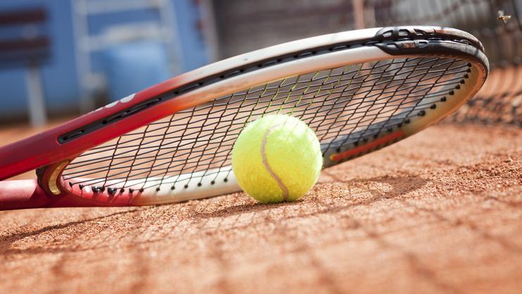 Tennisball liegt auf einem Platz neben einem Tennisracket auf dem Sandboden.